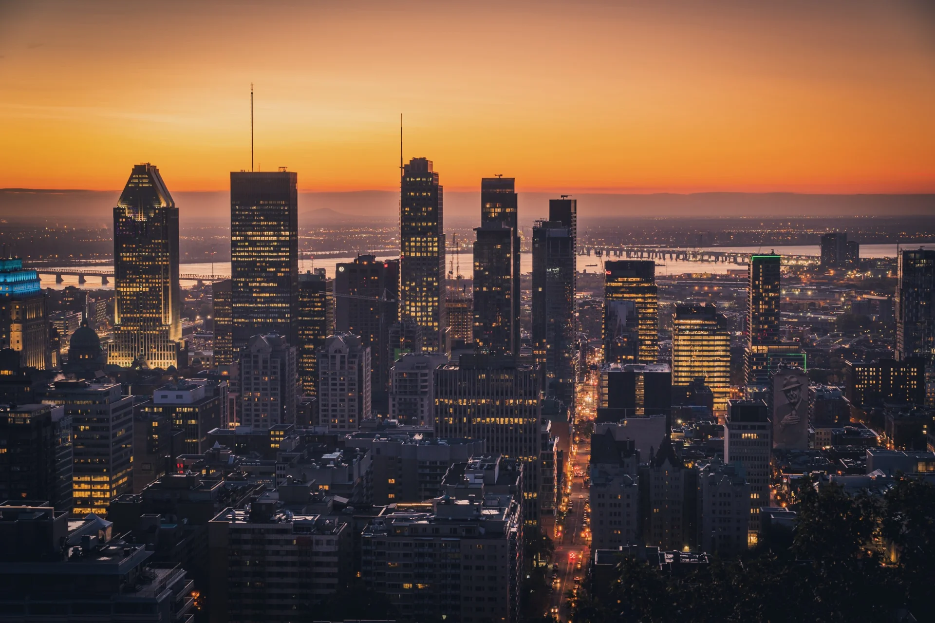 Le centre-ville de Montréal à la tombée de la nuit, sous un ciel orange, les fenêtres allumées.