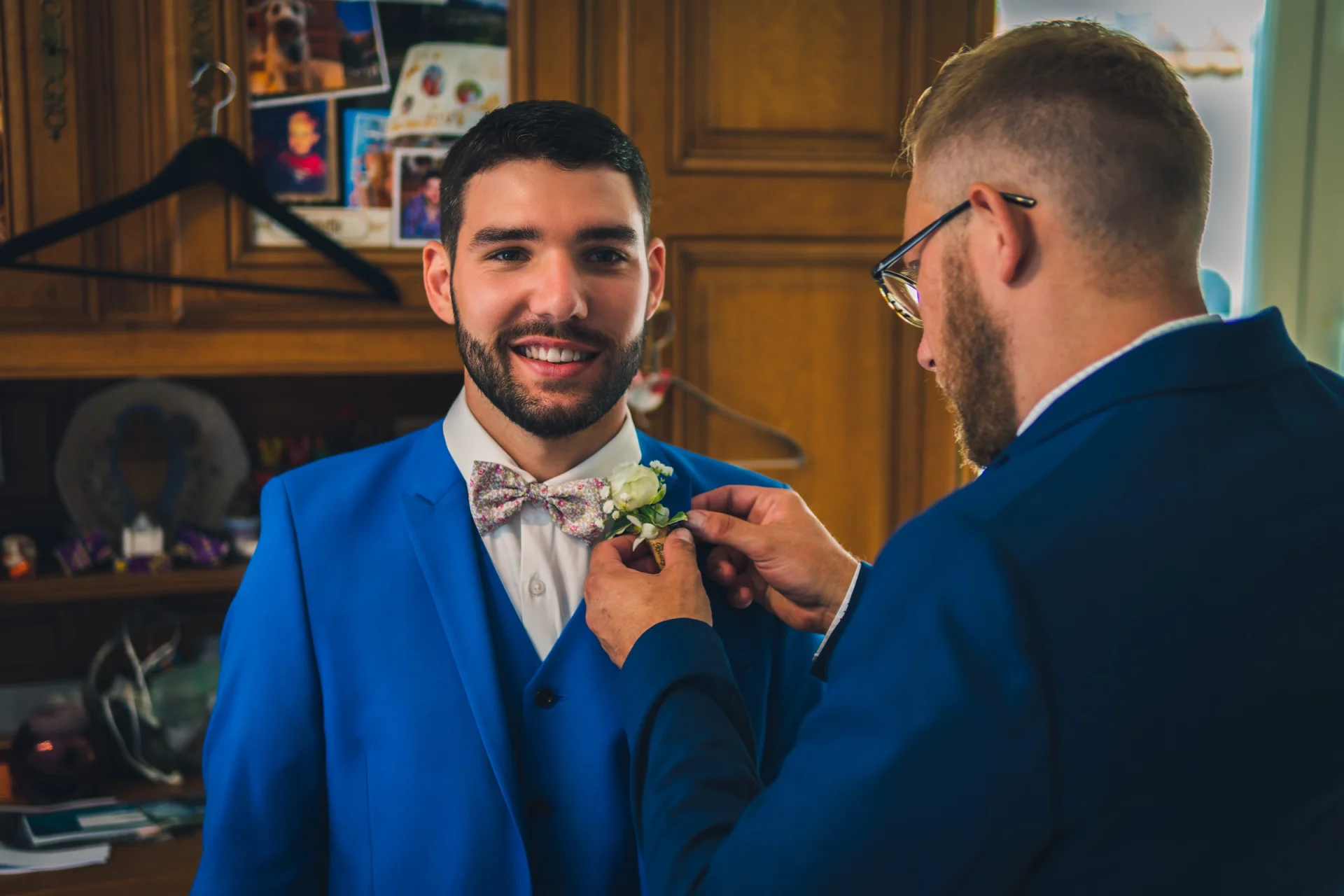 Un padrino ajusta el ojal del novio, ambos con traje azul.