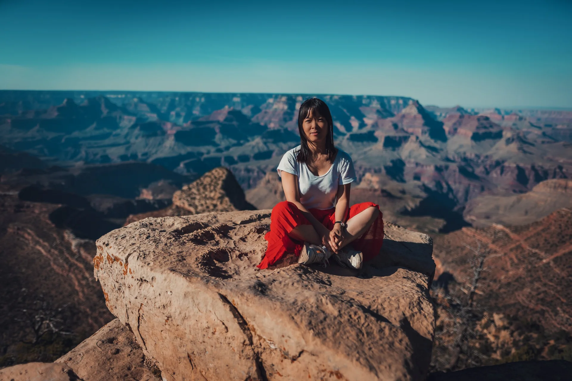 Une femme assise sur un rocher, le Grand Canyon derrière elle.