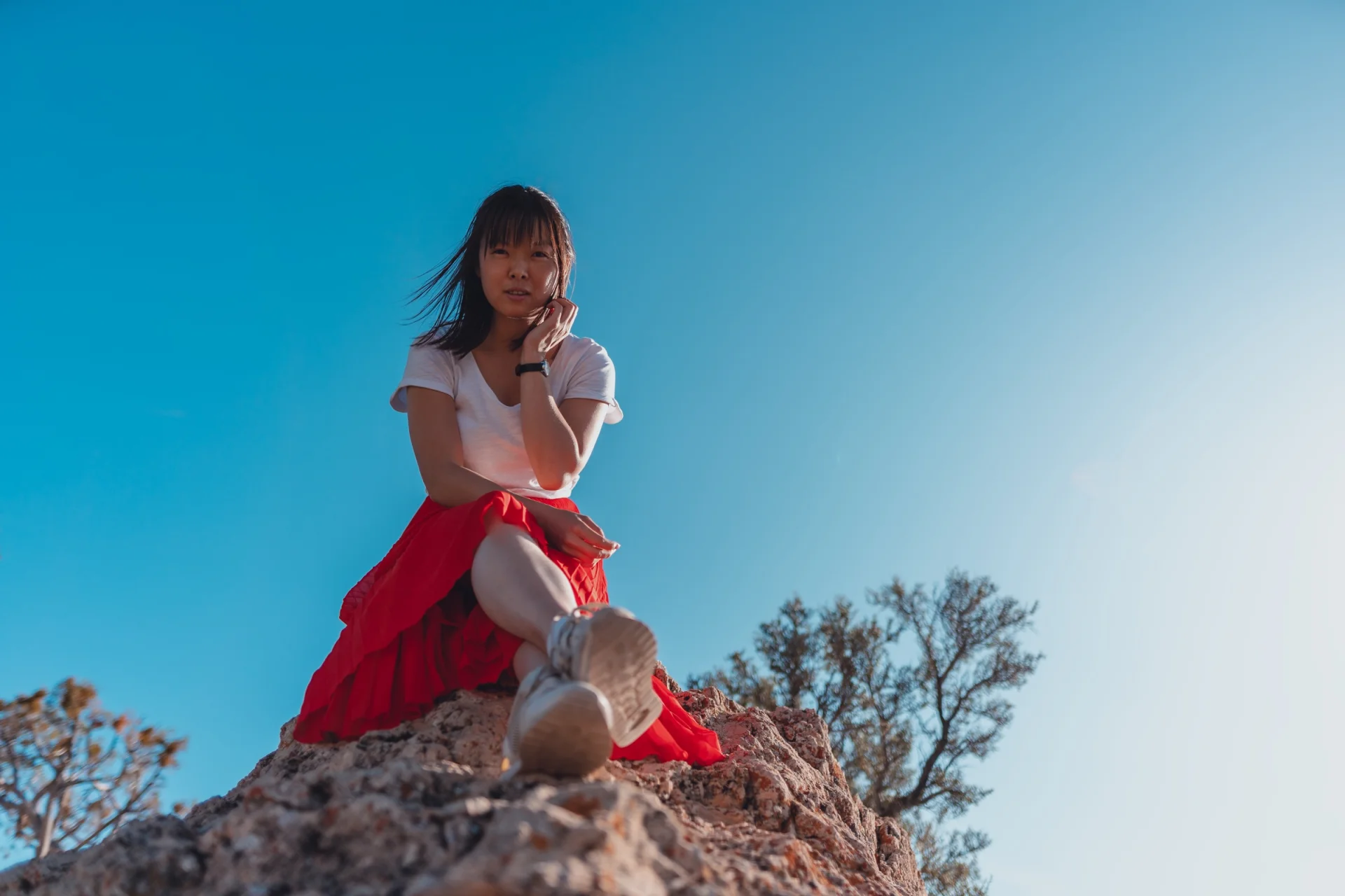 Una mujer sentada sobre una roca, recortada contra un cielo azul sin nubes.