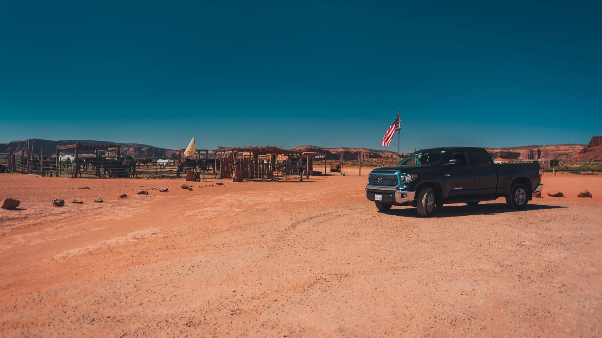 Una camioneta aparcada junto a una bandera estadounidense, al borde de una pista del desierto.