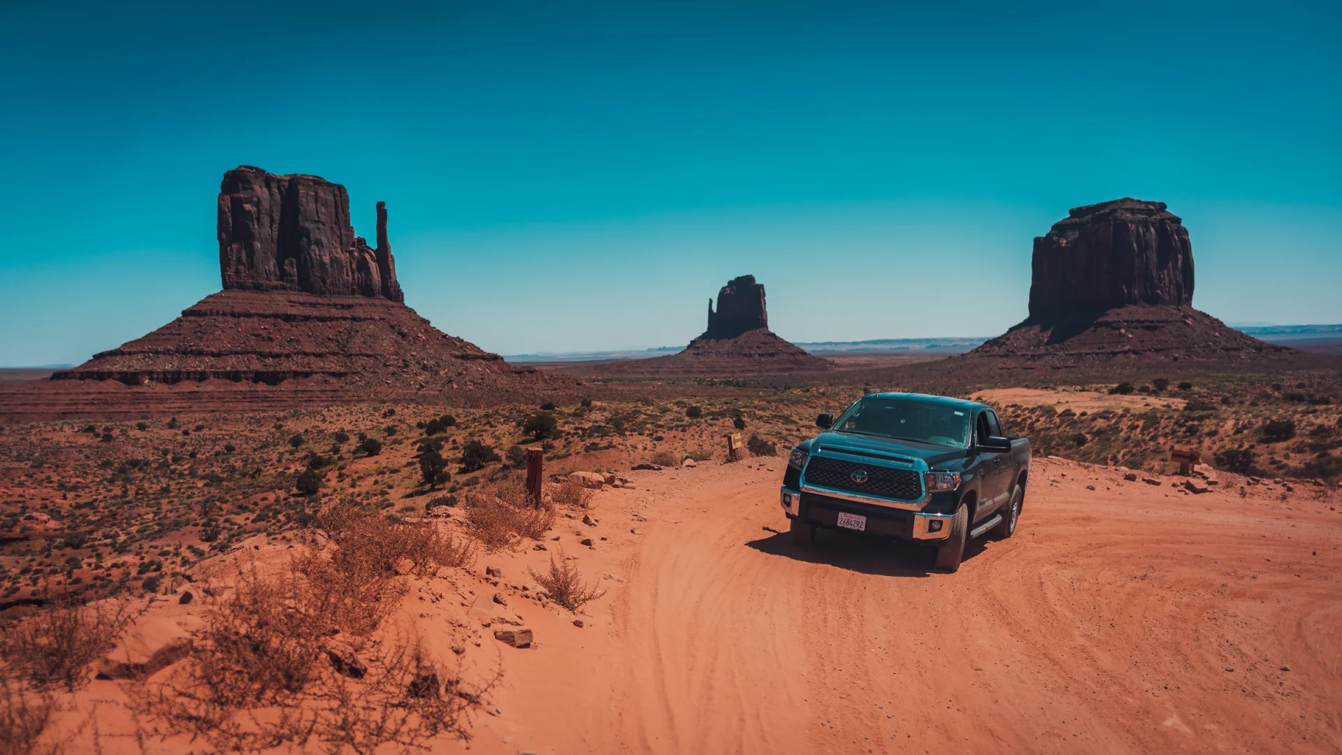 Una camioneta negra en la pista de tierra que cruza Monument Valley, entre dos cerros.