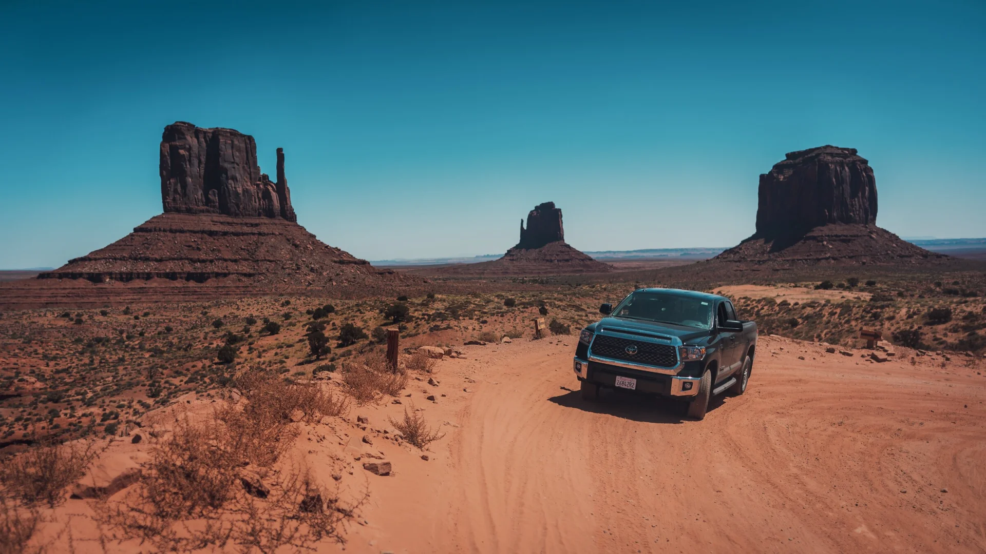 Un pick-up noir sur la piste de terre qui traverse Monument Valley, entre deux buttes.