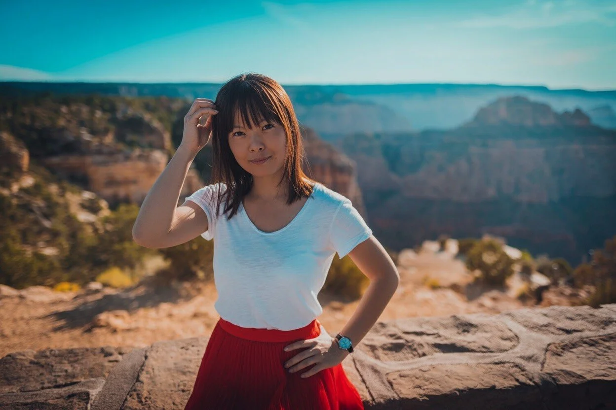Une femme en t-shirt blanc et jupe rouge devant les gorges du Grand Canyon.